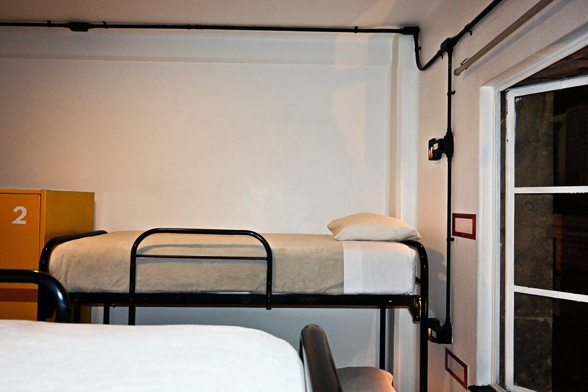Ein Etagenbett mit weißer Matratze und Kissen, ein Stuhl und eine Tür mit Fenster.