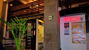 A reception area with a 'Welcome!' sign, a bulletin board with event listings, and a plant in the foreground. - Hostel Mundo Joven (Mexico City)