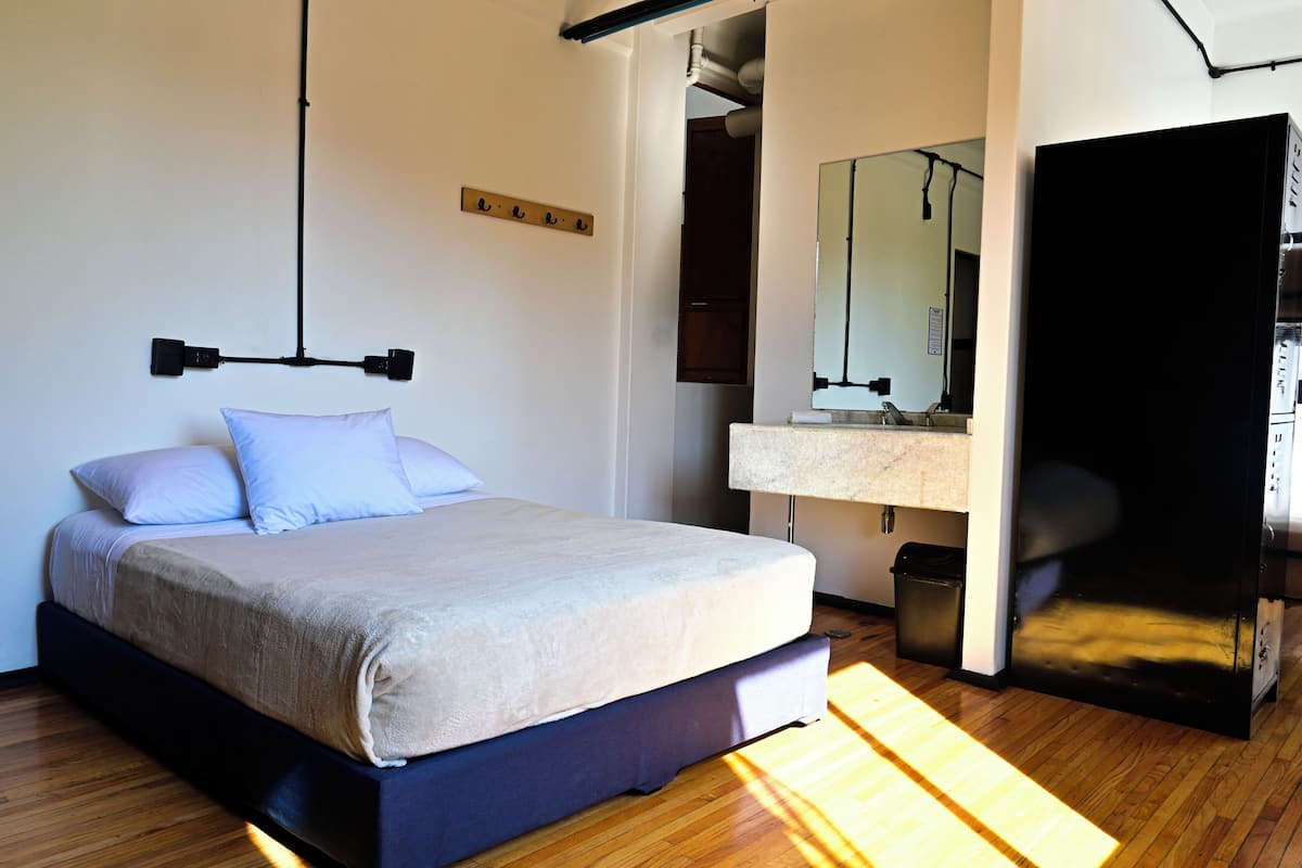 Ein modernes Schlafzimmer mit einem Bett, einer Pendelleuchte, einem Spiegel und einem schwarzen Kleiderschrank.