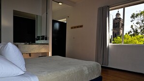 A hotel room with a large bed, a bathroom with a mirror, and a window with a view of a historic building. - Hostel Mundo Joven (Mexico City)