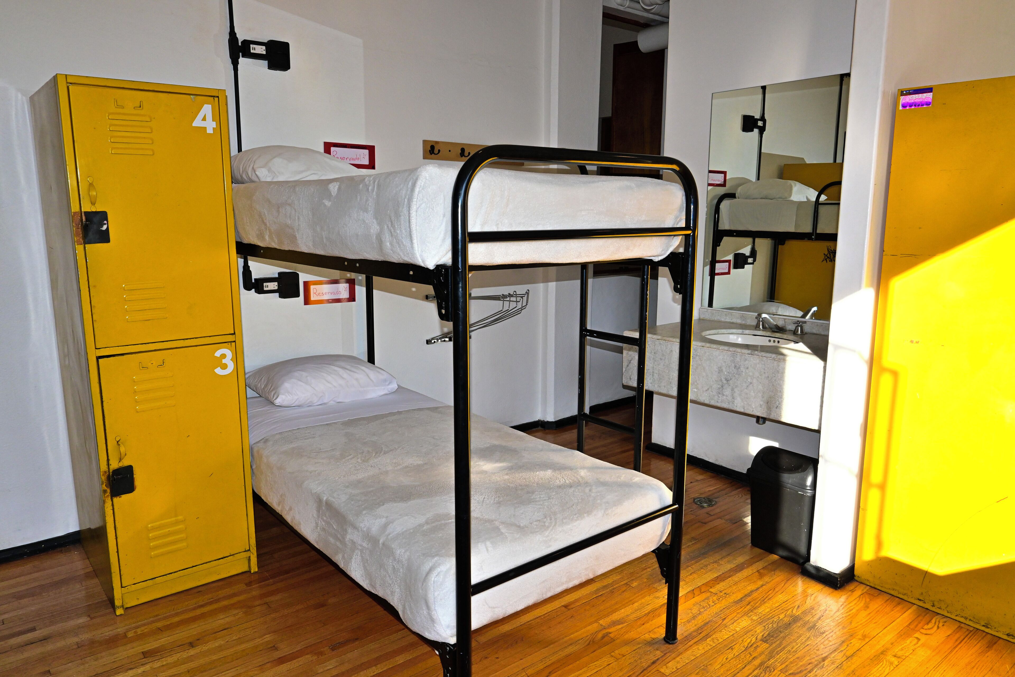 A dormitory room with bunk beds, a yellow storage unit, and a sink.