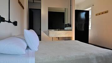 Habitación de hotel con cama, un espejo grande, un lavamanos y una puerta.