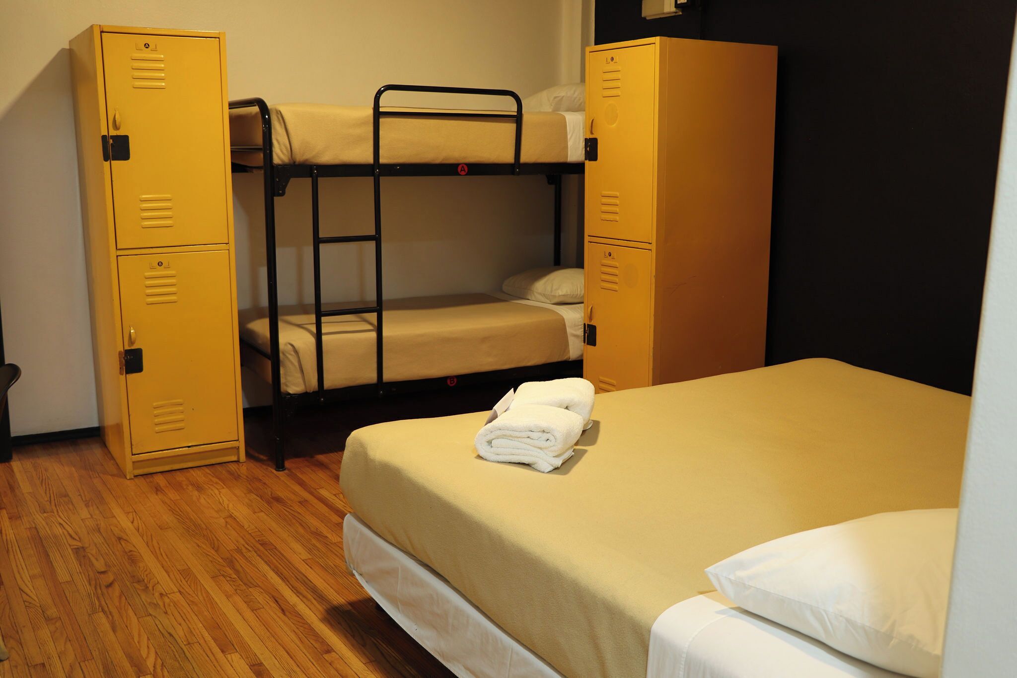 A dormitory room with bunk beds, two yellow lockers, and a neatly made bed.