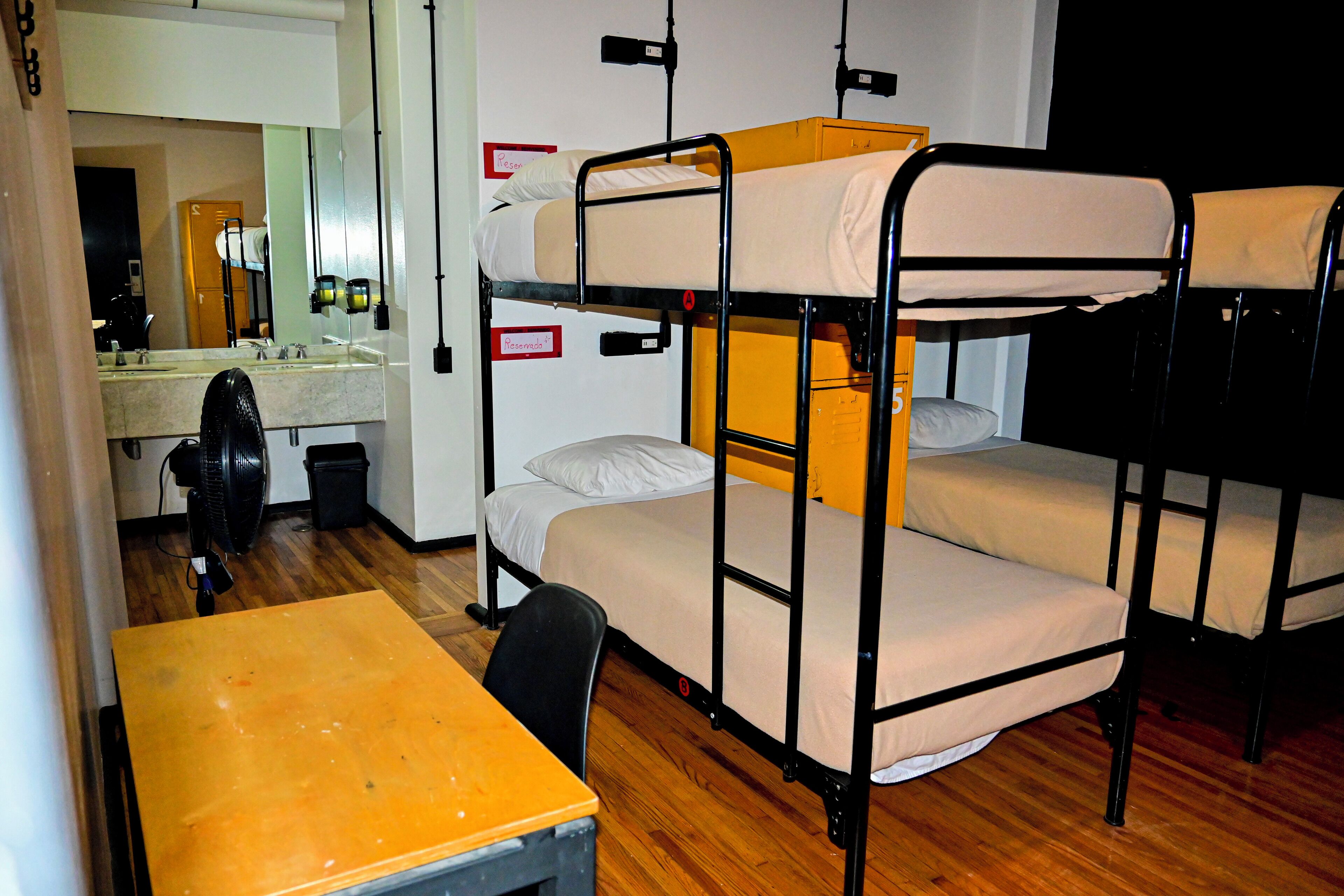 Un dormitorio con literas, un escritorio, una silla, un espejo y un lavamanos.