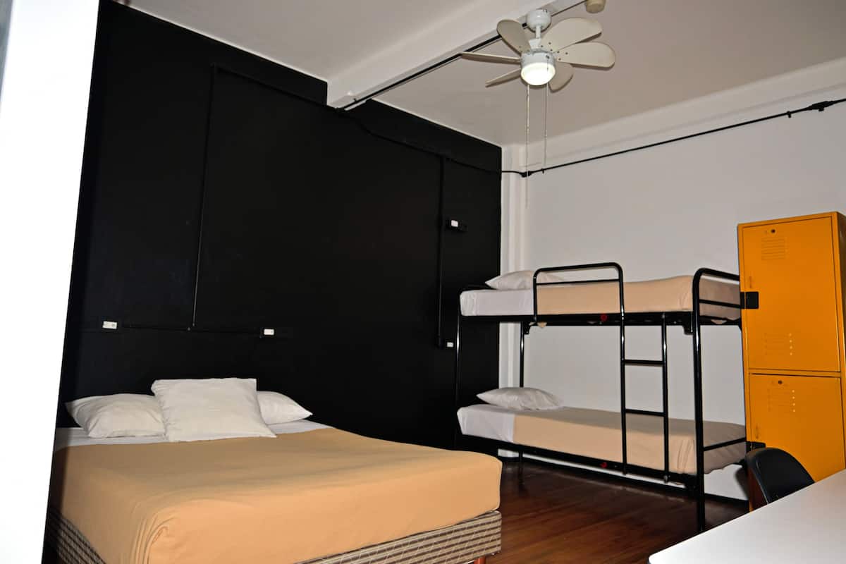 Ein Schlafraum mit Etagenbetten, Deckenventilator, Schreibtisch und einem gelben Stauraumschrank.
