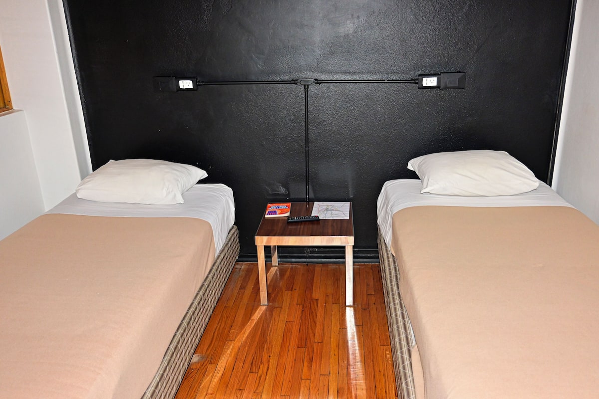 Ein Zimmer mit zwei Betten, einem kleinen Holztisch und einem schwarzen Kopfteil.