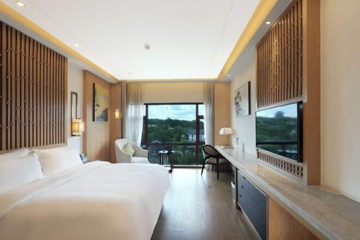 Une chambre d’hôtel avec un grand lit, un bureau, une chaise, une télévision et une vue sur l’extérieur.