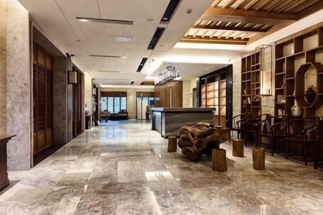 A hotel lobby with a marble floor, wooden furniture, and a reception desk.. Huazhushan Hotel