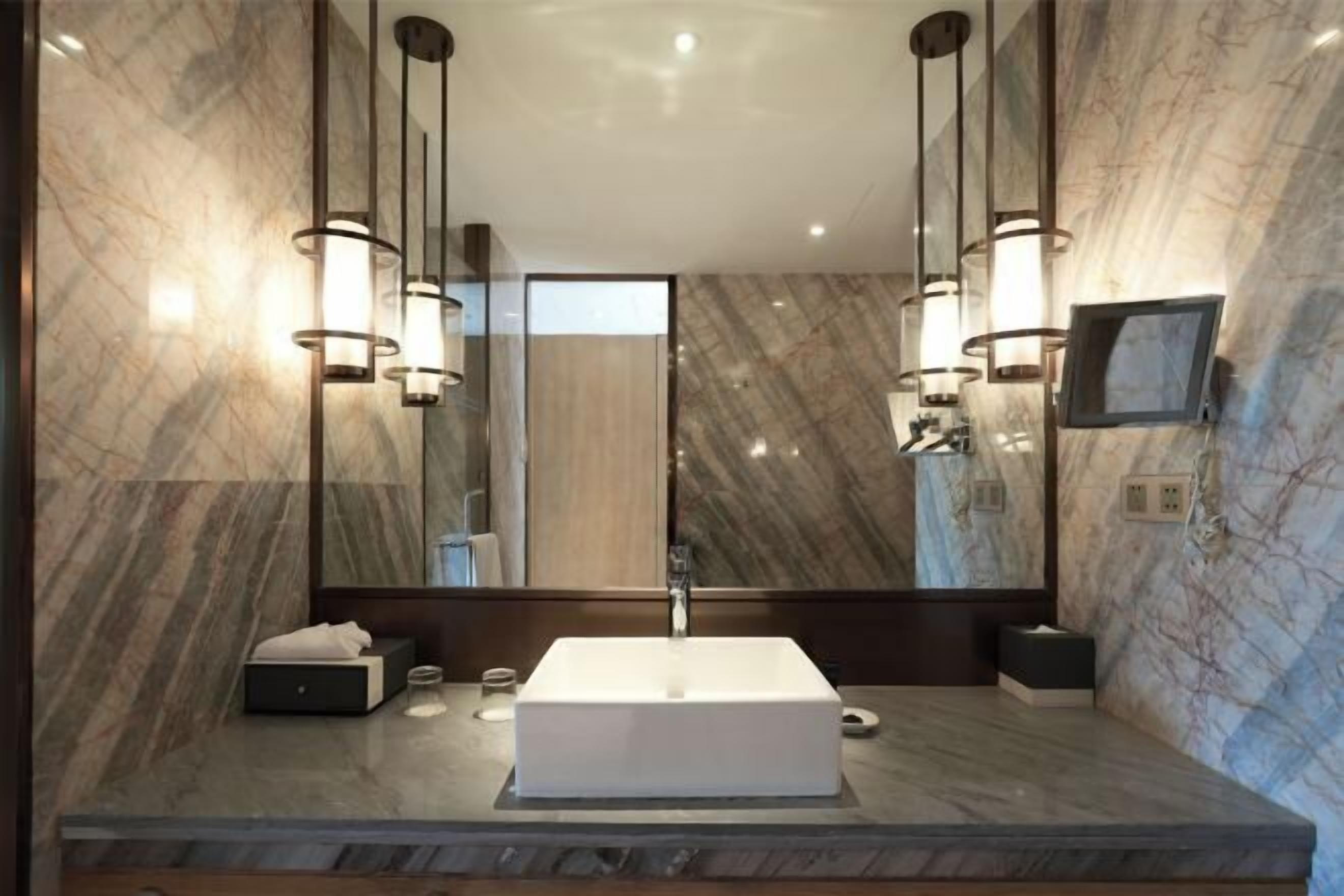 A modern bathroom with a large mirror, a white sink, and pendant lighting.