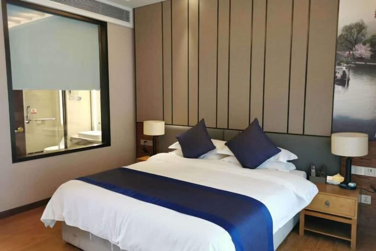 Une chambre d’hôtel avec un grand lit, une fenêtre, une tête de lit en bois et une table de chevet avec une lampe.