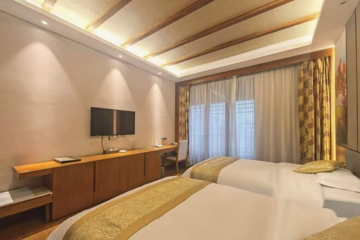 Une chambre d’hôtel avec deux lits, un bureau, une télévision et une fenêtre avec des rideaux.