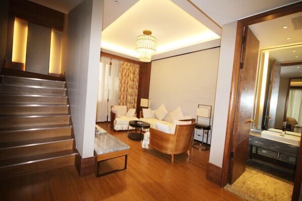A modern hotel room with a wooden staircase, a sofa set, a coffee table, and a large mirror.