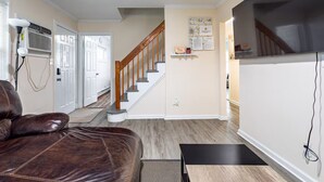 Un salon avec un canapé en cuir marron, un escalier et un téléviseur fixé au mur.