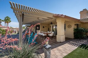Un patio couvert avec une table et des chaises, une pergola et une vue sur un quartier résidentiel bordé de palmiers.