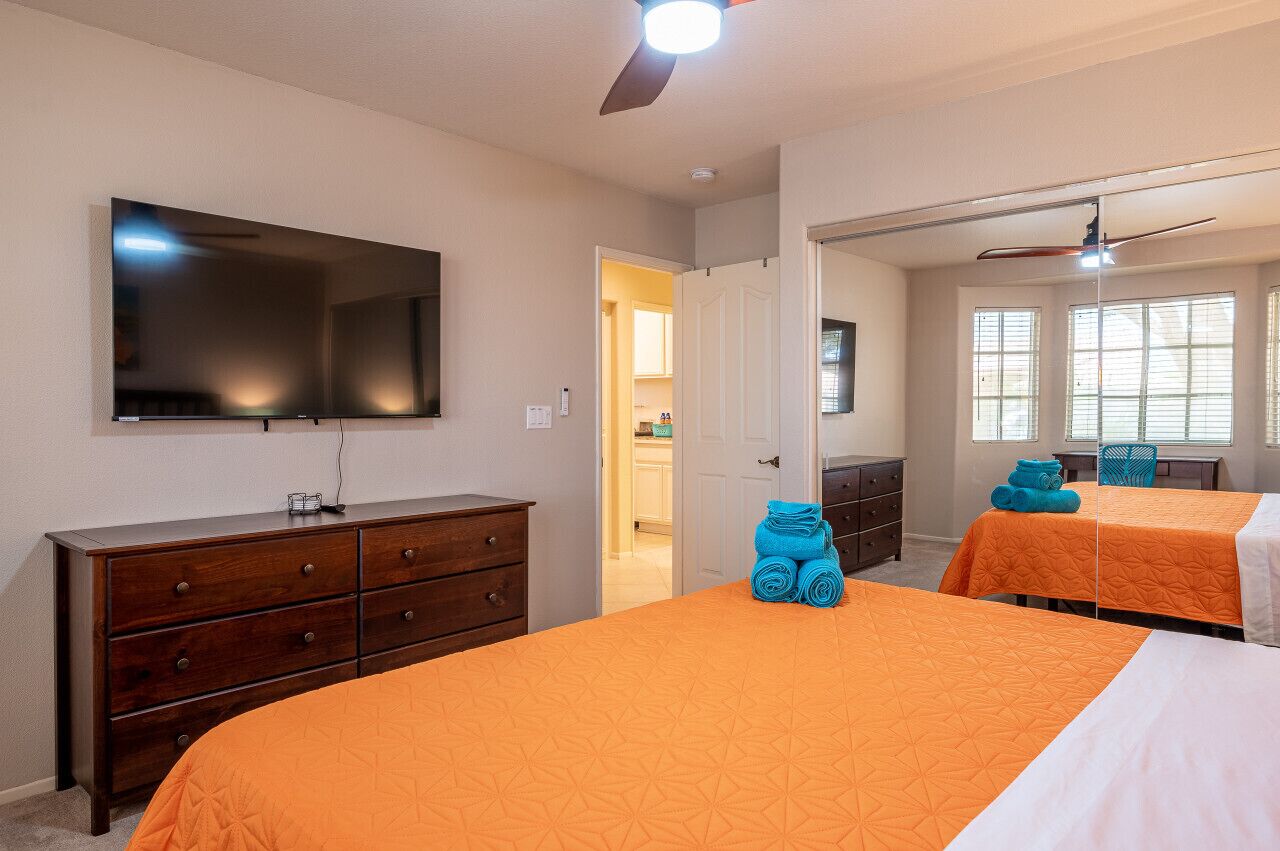 A hotel room with two beds, a TV, a dresser, and a ceiling fan.