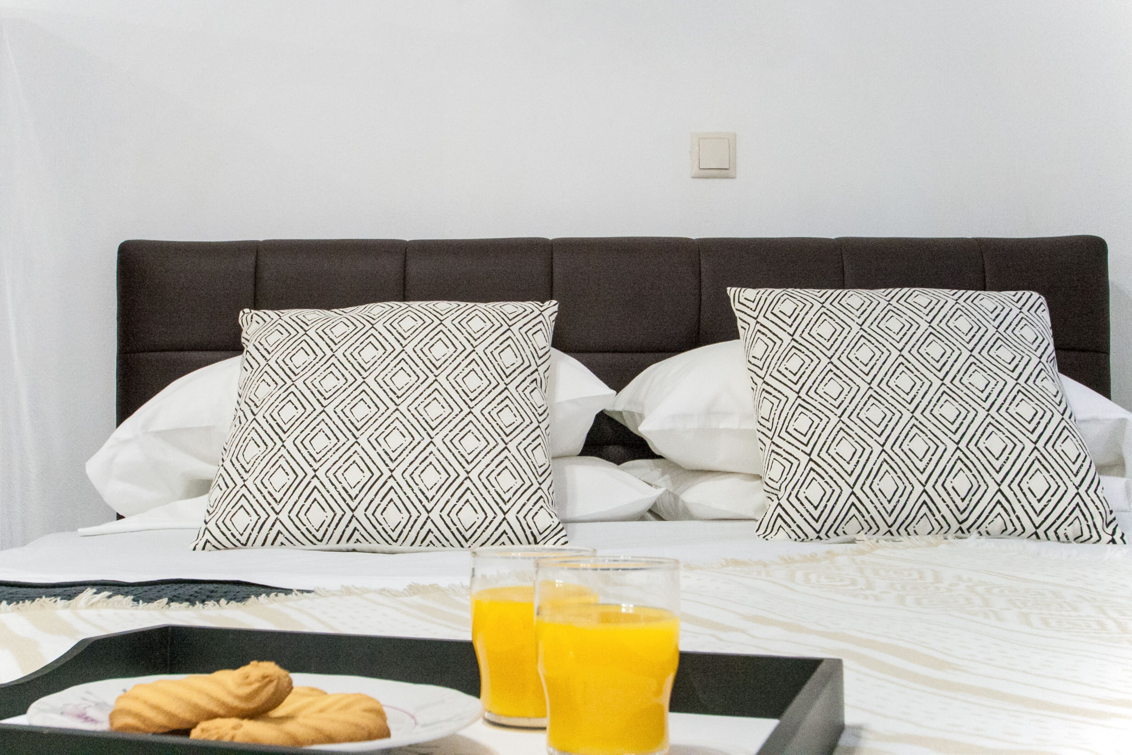 Un lit avec des coussins à motifs, un plateau avec des croissants et du jus d’orange, et un couvre-lit blanc.