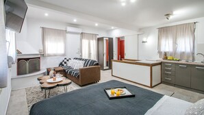 Ein modernes Hotelzimmer mit Bett, einer Sitzecke, einem kleinen Essbereich und einer Küchenzeile.
