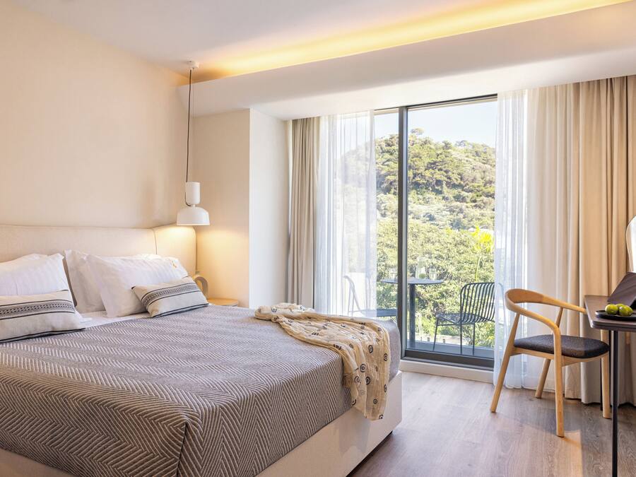 Habitación de hotel moderna con una cama grande, un escritorio con una computadora portátil y vistas al exterior.