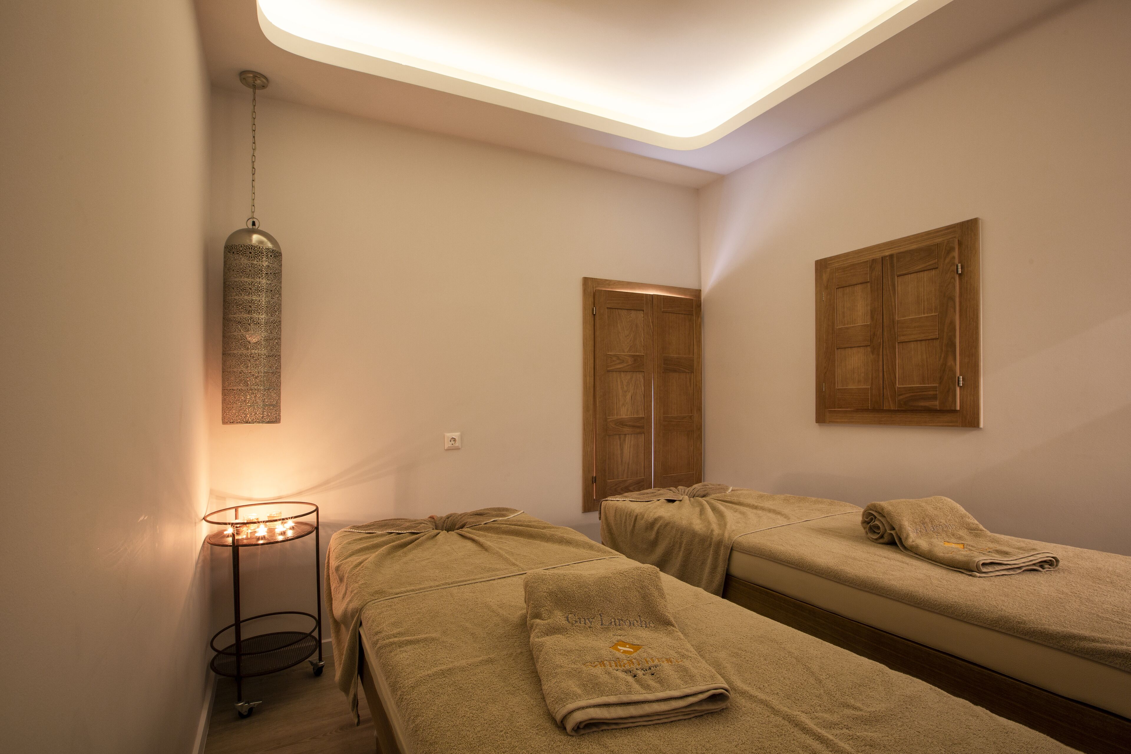 Une chambre avec deux lits, une petite table avec des bougies et un luminaire suspendu.