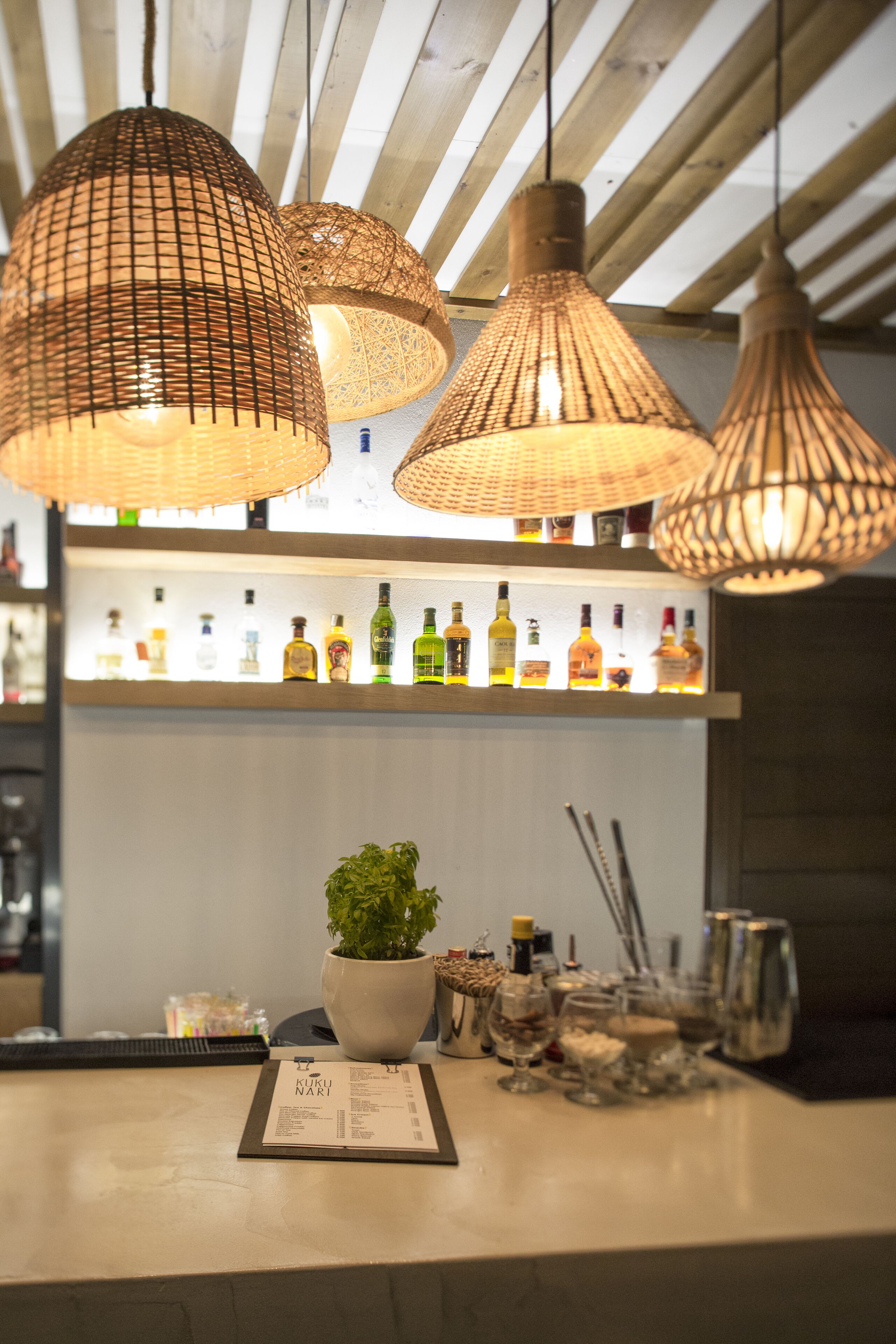 Een bar met hangende rieten lampen, een potplant en een menu op de toonbank.