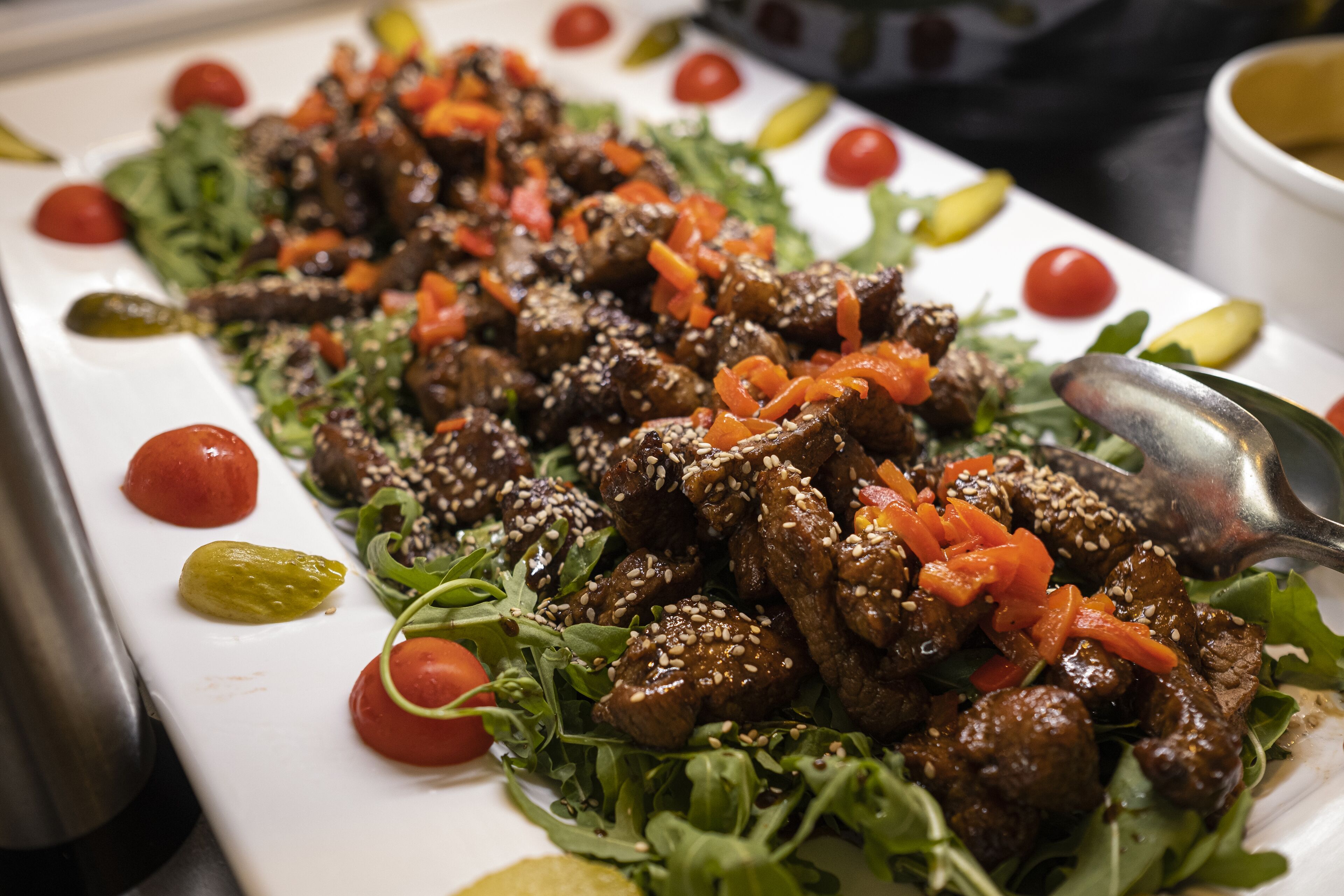 Un plato de carne con semillas de sésamo y zanahorias, adornado con tomates cherry y lechuga.