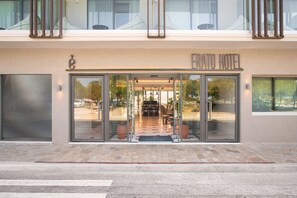 The entrance of the Frato Hotel with a glass door, a visible outdoor seating area, and a balcony above. - Erato by Samian Mare (Samos)