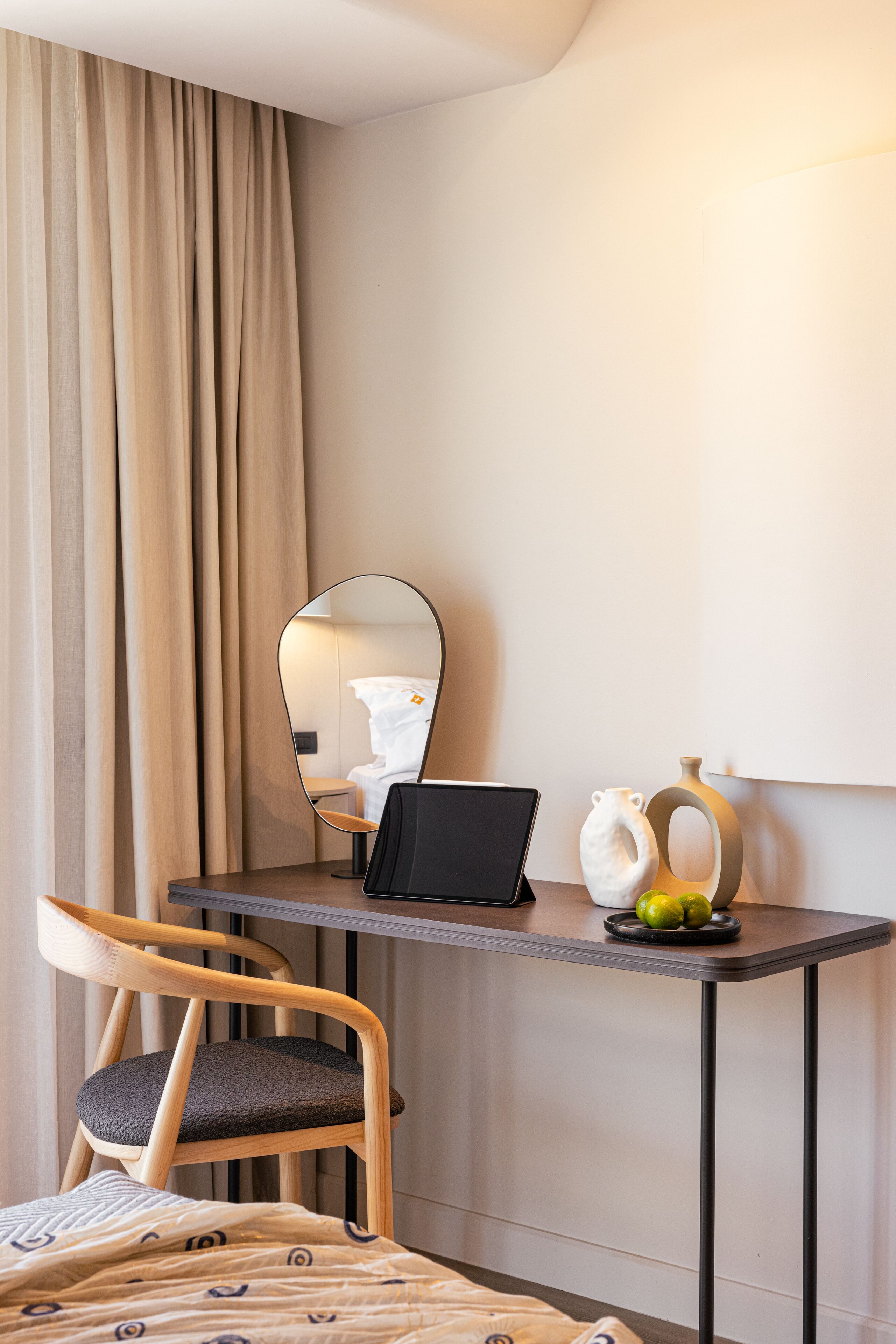 Ein Hotelzimmer mit einem Bett, einem Holzstuhl, einem Schreibtisch mit einem Laptop, einem Spiegel und dekorativen Vasen.
