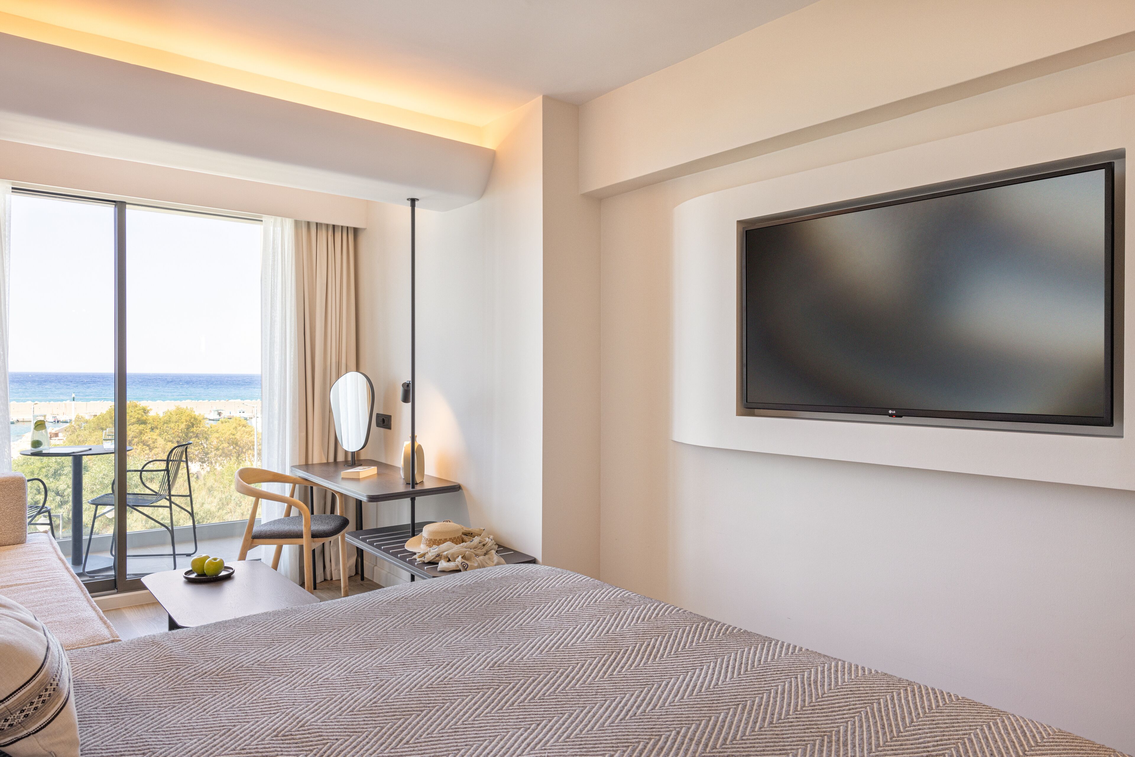 A hotel room with a bed, a desk, a chair, a television, and a view of the ocean.