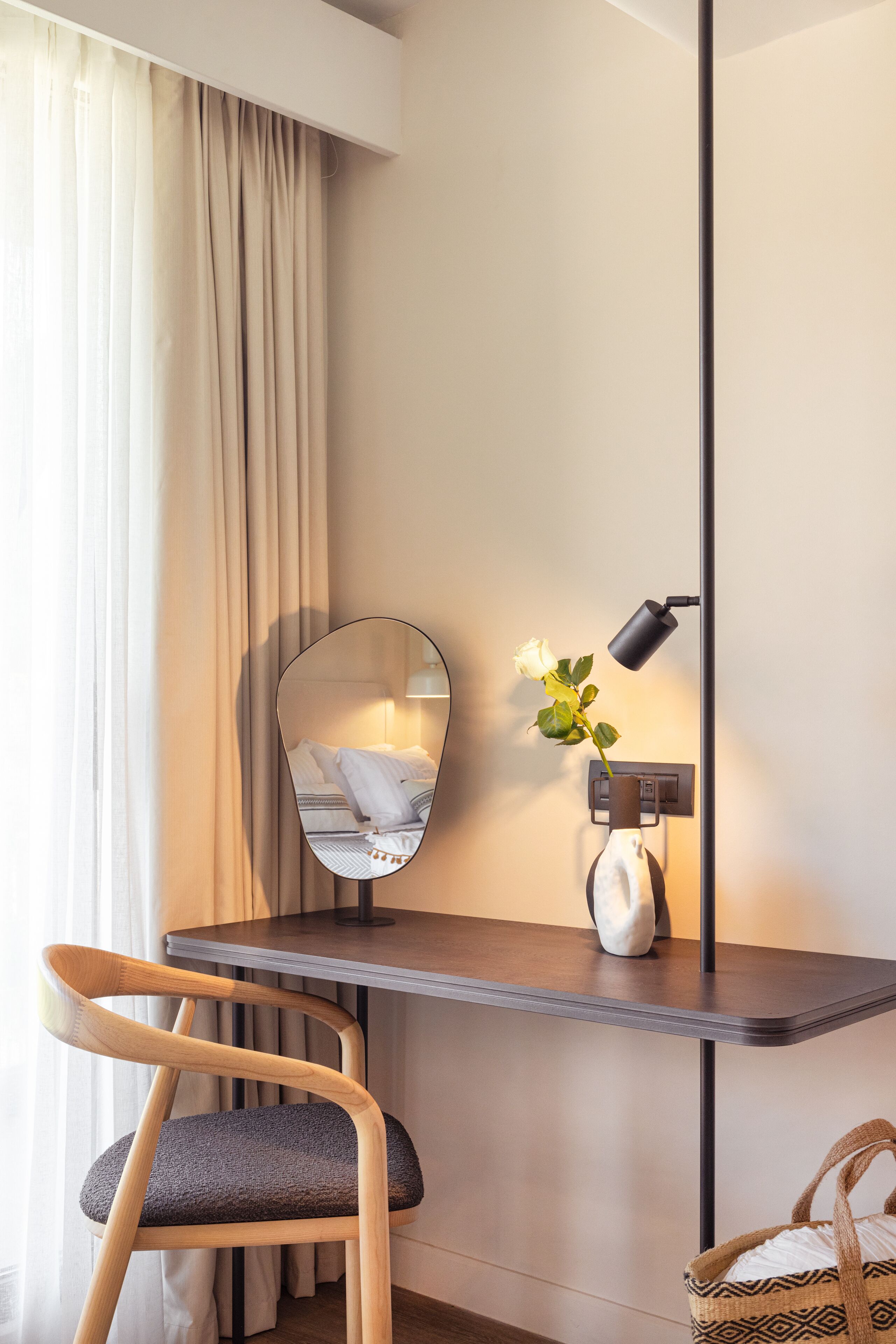 Una habitación moderna con escritorio, silla y espejo adherido a la pared que refleja una cama.