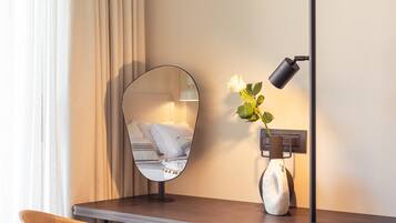 Una habitación moderna con escritorio, silla y espejo adherido a la pared que refleja una cama.