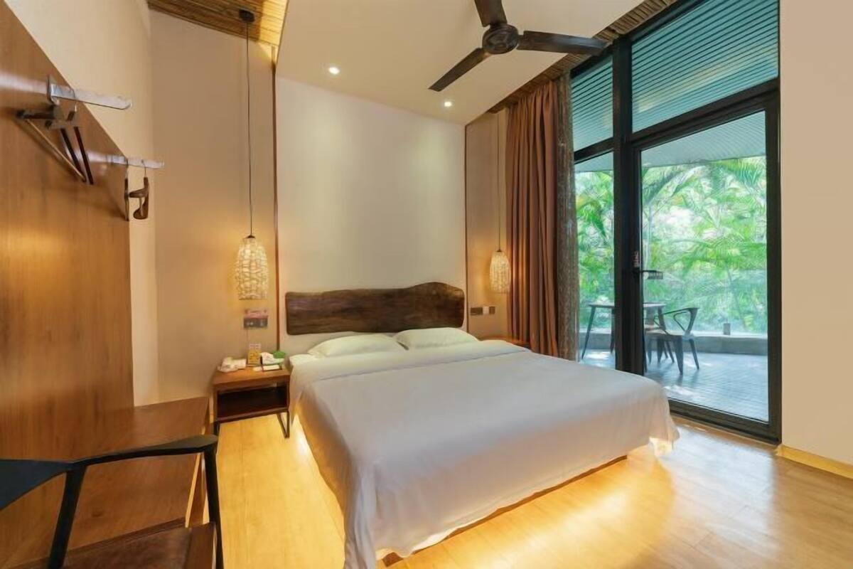 Un dormitorio con cama, escritorio, ventilador de techo, mesita de noche y ventana con vistas a zonas verdes.