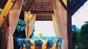 An outdoor dining area with tables set for a meal, draped with white curtains, and decorated with blue balloons. - Vaikuha Seaview Hotel (Beihai)