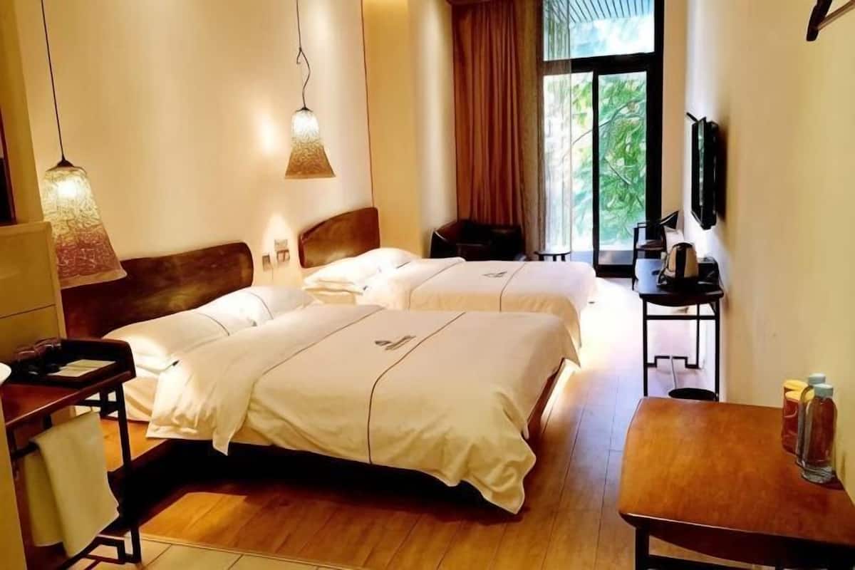 A hotel room with two beds, a desk, a chair, a TV, and a window with a view.