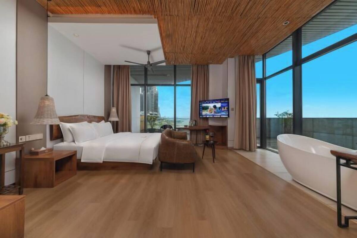 Una habitación de hotel moderna con una cama grande, una zona de estar, una bañera y un televisor.
