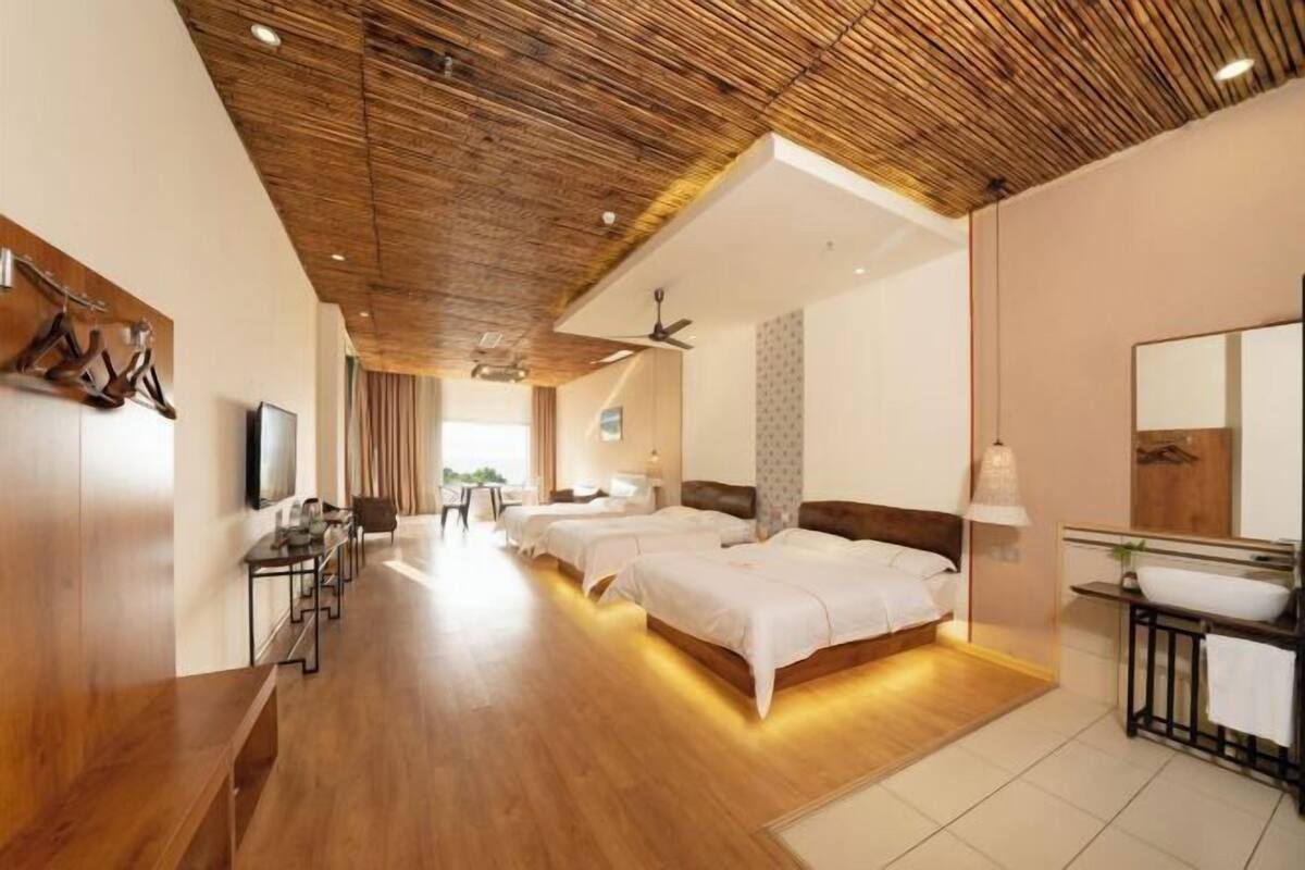 Habitación de hotel con techo de madera, cama, escritorio, televisor y baño con espejo y lavamanos.
