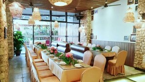 A long dining table with pink floral centerpieces, surrounded by cushioned chairs with light-colored covers. - Vaikuha Seaview Hotel (Beihai)