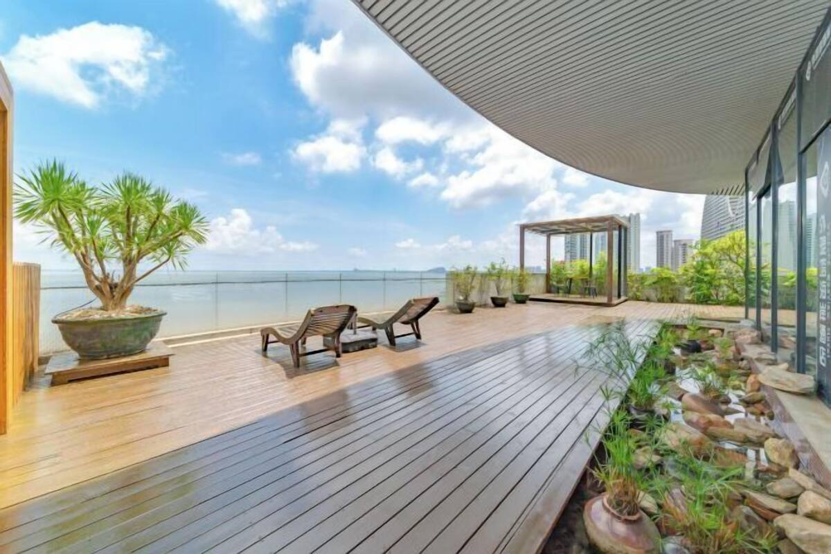 Una terraza de madera con sillones de descanso, un cerramiento de cristal y vista al mar.