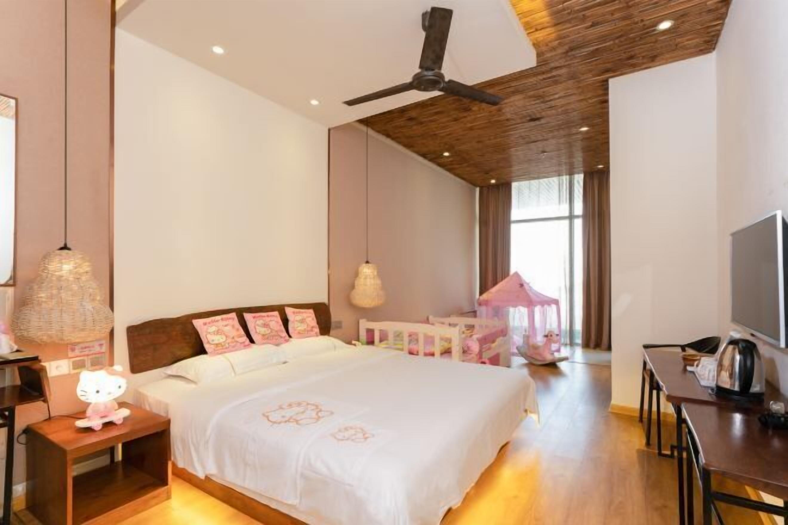 A bedroom with a bed, bedside table, lamp, ceiling fan, and a TV.