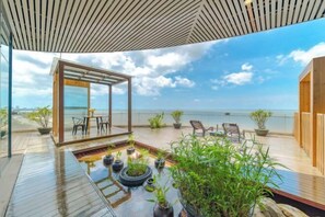 A wooden deck with a glass enclosure, potted plants, and a view of the sea.