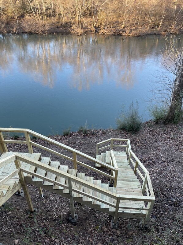 A wooden staircase leading to a dock over a calm body of water, surrounded by leaf-covered ground and bare trees.