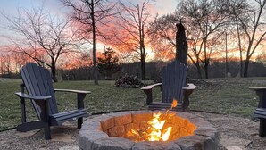 A stone fire pit with two Adirondack chairs and a stack of firewood. - Relax and Unwind on the Caddo River in Beautiful Arkansas! Book now! (Amity)