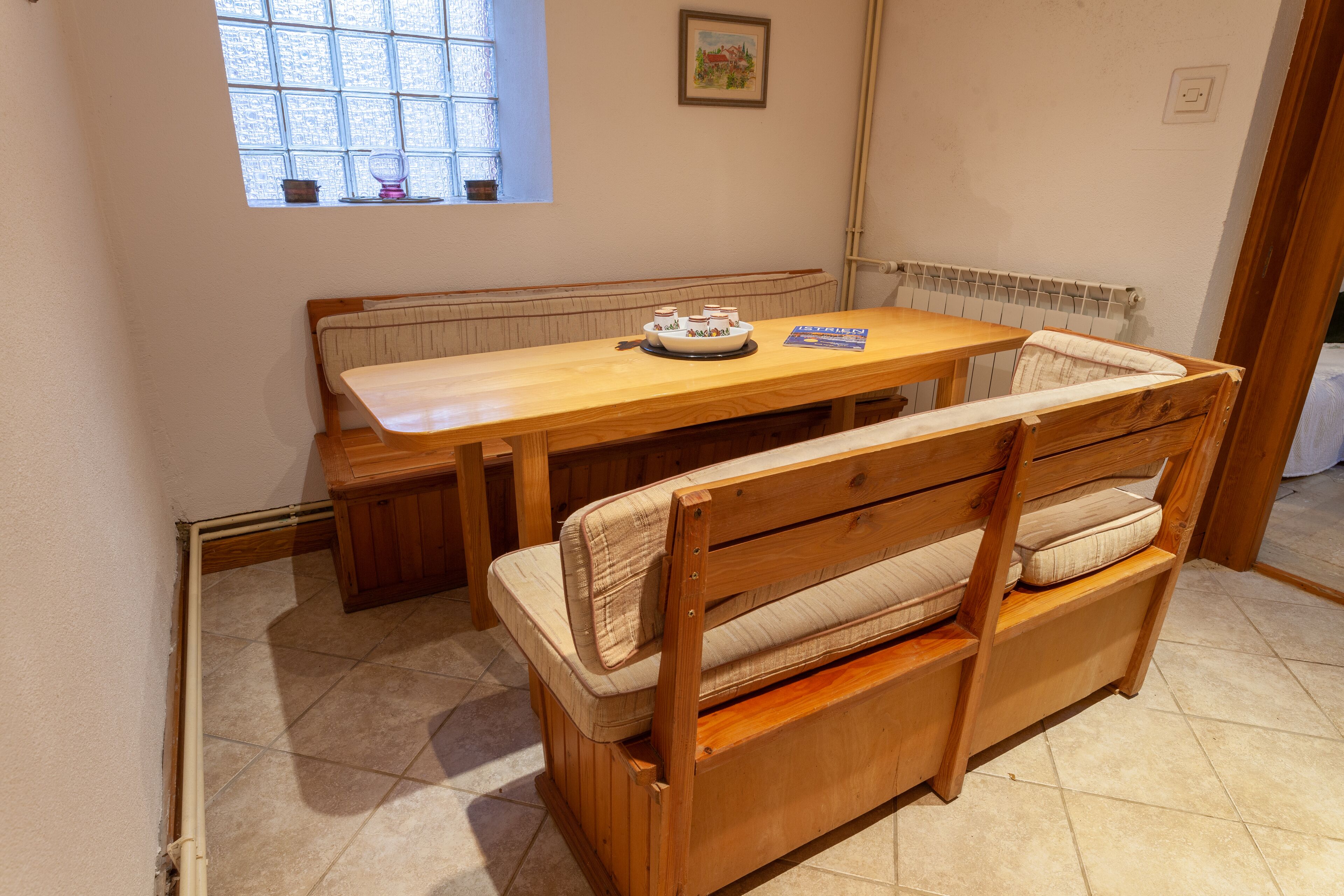 A wooden dining table with benches, a window with a view, and a radiator.