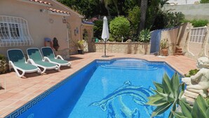 Una piscina con un mosaico de delfín, rodeada de sillones de descanso y plantas en macetas.