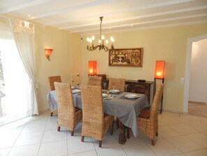 Ein Esszimmer mit einem für sechs Personen gedeckten Tisch, umgeben von Korbstühlen, einer Kristallleuchter und zwei Wandlampen.