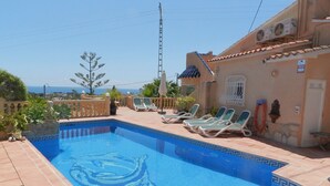 Uma piscina com design de golfinho, rodeada por espreguiçadeiras e vista para o mar.