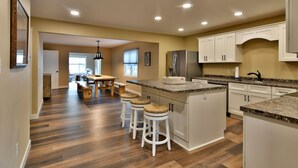 Una cocina moderna con una isla central, taburetes de bar y un comedor con mesa y sillas de madera.