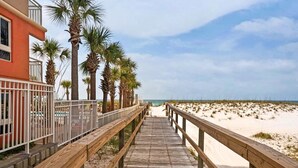 A wooden boardwalk leading to a beach with palm trees and a building on the left. - 🌅Walk2Beach | St. Martin Beachwalk Villas 423 (Destin)