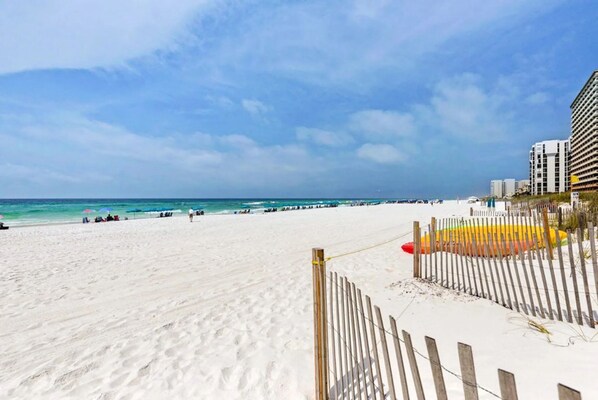 A beach with a wooden fence, a pier, and buildings in the background.