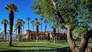 A resort with palm trees, a pond, and a building with a tiled roof.