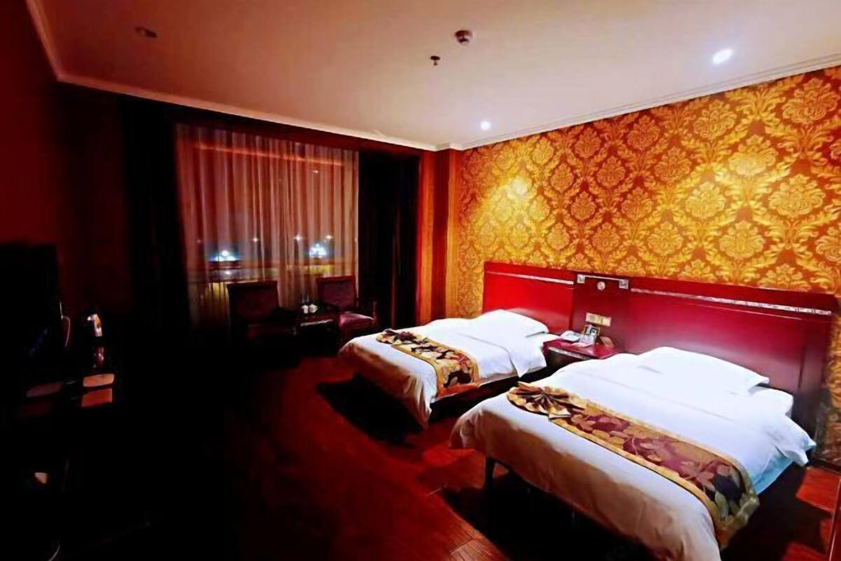 A hotel room with two beds, a large window with curtains, and a patterned wall.